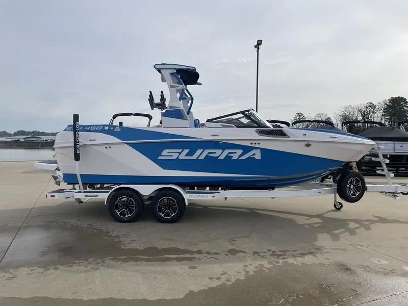 Slide: The Image of 2023 Supra SUPRA SA 450 boat on trailer, blue and white design, parked outdoors. - 5