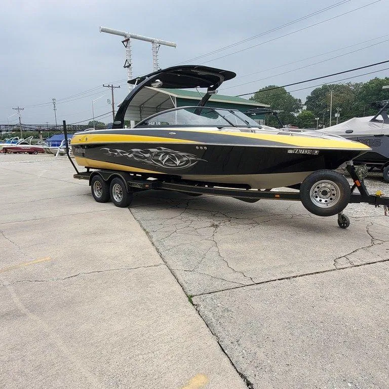 Slide: The Image of 2006 Malibu 23 LSV boat on trailer, black and yellow design, parked outdoors. - 2
