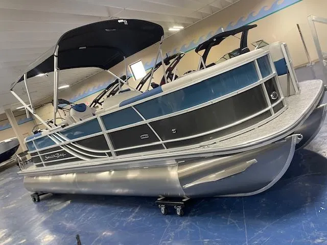 Slide: The Image of 2025 South Bay LE pontoon boat in showroom, featuring sleek design and blue accents. - 2