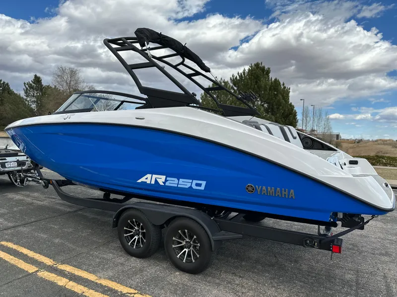 Slide: The Image of 2025 Yamaha AR250 boat on trailer, blue and white design, parked outdoors under cloudy sky. - 2