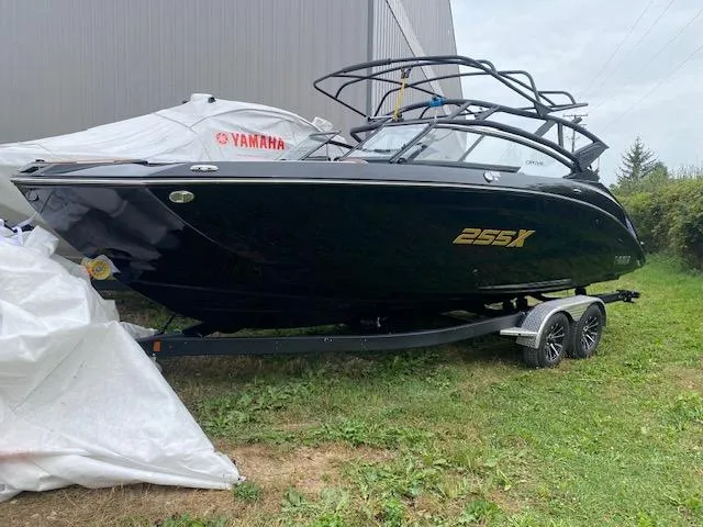 Slide: The Image of 2025 Yamaha Boats 255XD, black, on trailer near building, partially covered. - 0