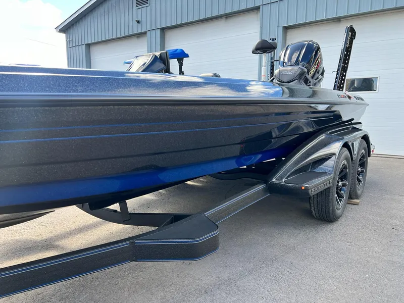 Slide: The Image of 2025 Skeeter FXR21 LE boat on trailer, parked outside a garage. - 25