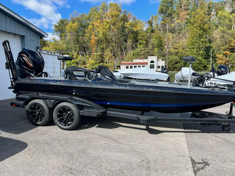 Slide: The Image of 2025 Skeeter FXR21 LE boat on trailer, parked outdoors, surrounded by trees. - 33