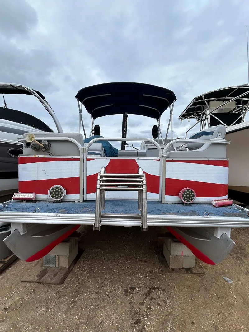 Slide: The Image of 2003 Starcraft 200 Fish Pontoon boat with red and white stripes, docked on land. - 15