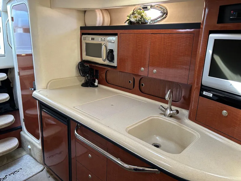 Slide: The Image of 2005 Sea Ray 340 Sundancer interior kitchen with sink, microwave, and wooden cabinetry. - 12