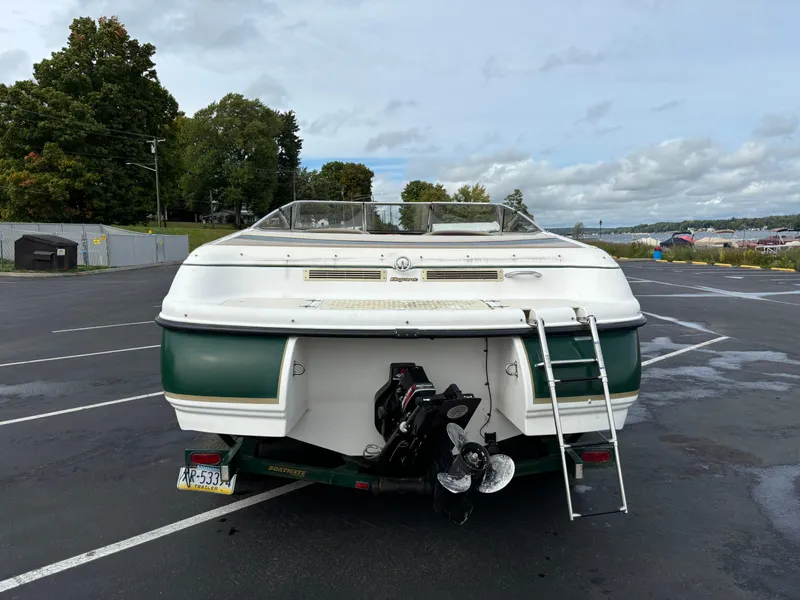Slide: The Image of 2002 Bryant 214 boat with ladder, parked in a lot, trees and cloudy sky in background. - 10