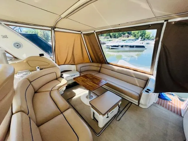 Slide: The Image of 1999 Sea Ray 460 Sundancer interior with tan leather seating and wooden table, docked by the water. - 10