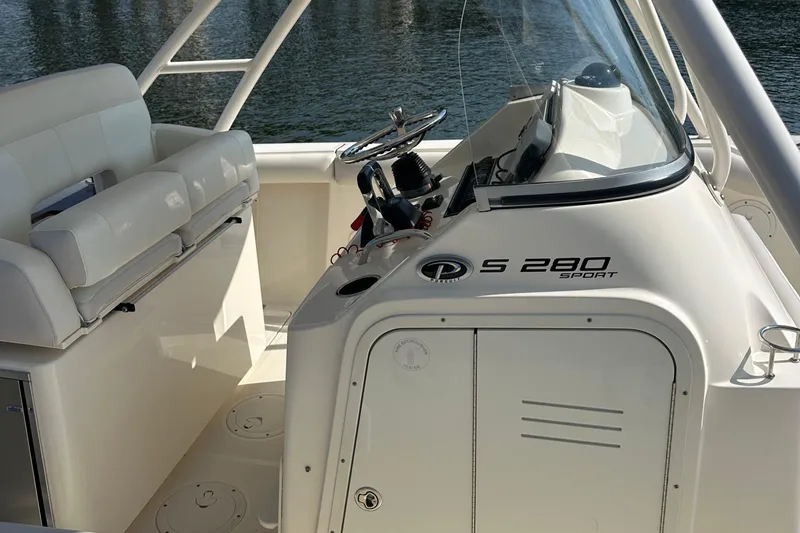 Slide: The Image of 2014 Pursuit S 280 Sport boat interior with steering wheel and seating, docked on water. - 16
