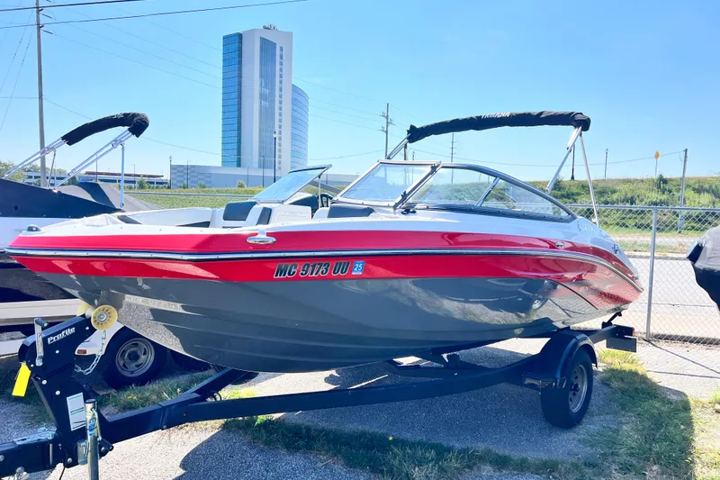 Slide: The Image of 2021 Yamaha Boats SX195 on trailer, red and gray, parked outdoors near a tall building. - 5