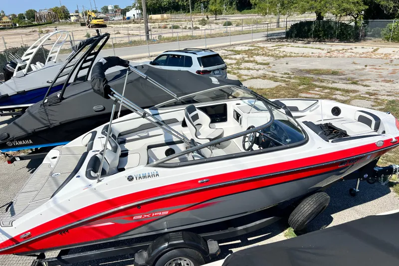 Slide: The Image of 2021 Yamaha Boats SX195, red and white, parked on a trailer in a lot. - 7
