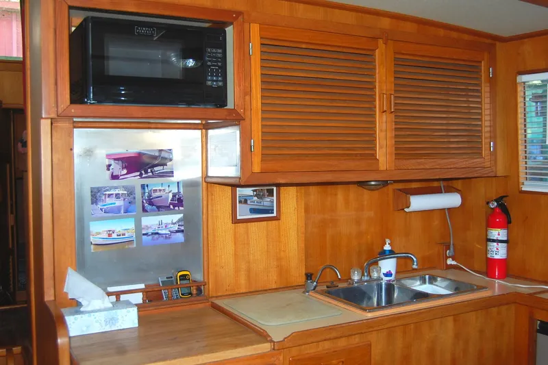 Slide: The Image of 1985 Sundowner Tug Princess Louisa kitchen with wooden cabinets, microwave, sink, and fire extinguisher. - 17