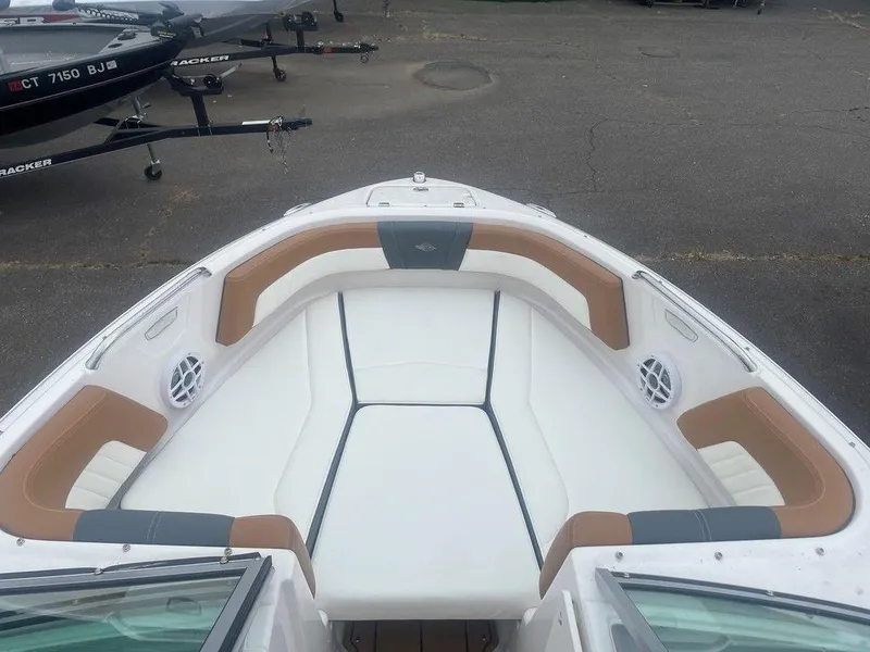 Slide: The Image of 2023 Chaparral 21 SSi boat interior with white and tan seating, docked on pavement. - 12