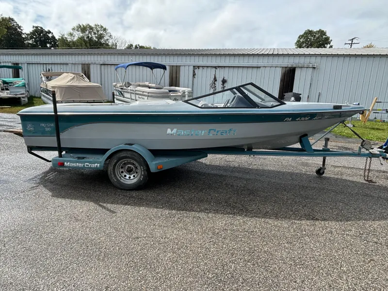 The Image of 1989 MasterCraft ProStar 190 boat on trailer, parked outdoors near a storage facility. - 0