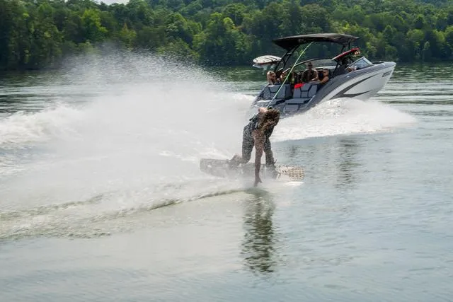 Slide: The Image of 2025 Yamaha Boats 255XE towing a wakeboarder on a scenic lake. - 4