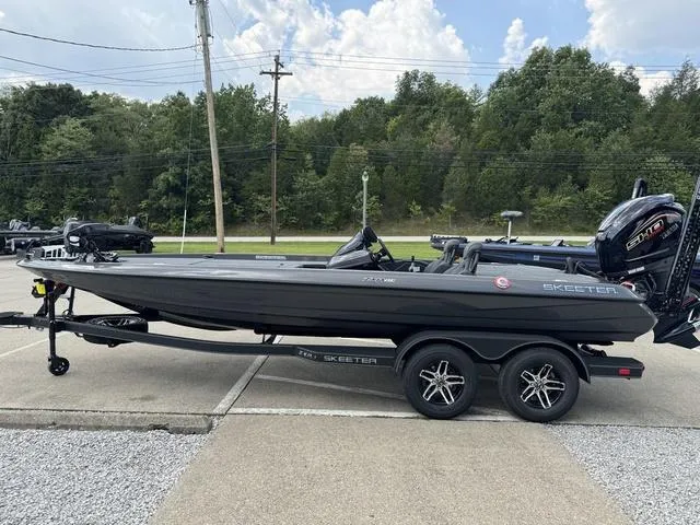 Slide: The Image of 2025 Skeeter ZXR21 boat on trailer, parked outdoors with trees in background. - 19
