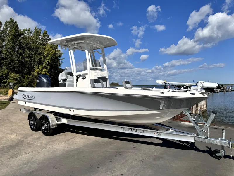 Slide: The Image of 2025 Robalo 226 Cayman boat on trailer by a lake under blue sky. - 1