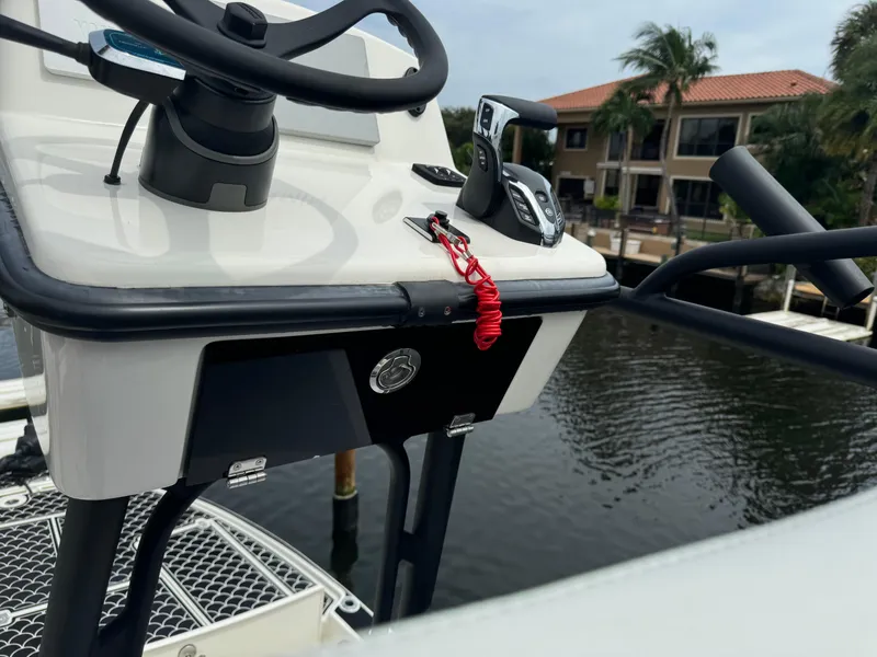 Slide: The Image of 2024 Pathfinder 2500 Hybrid boat console with steering wheel and controls, docked by waterfront homes. - 19