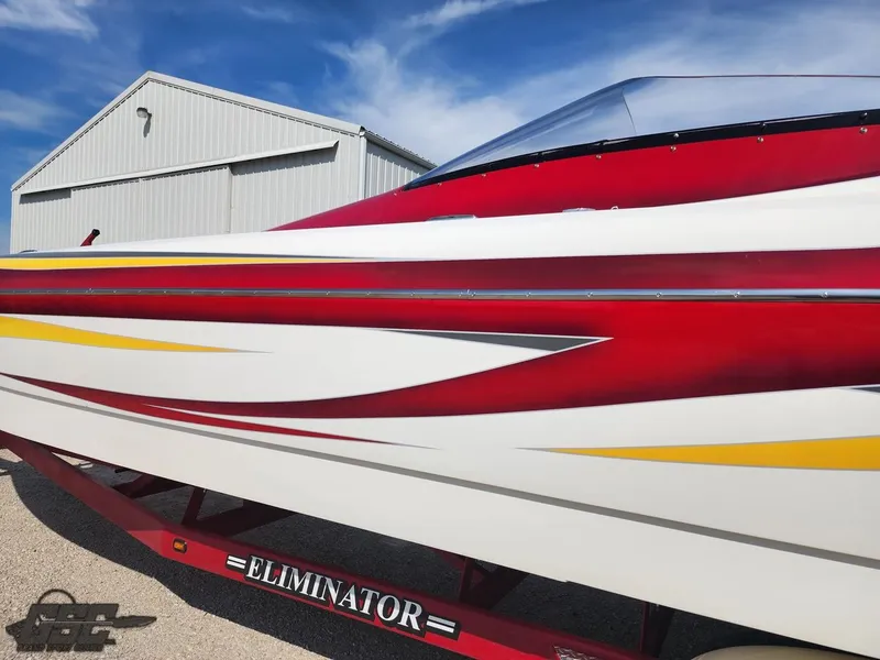 Slide: The Image of 2005 Eliminator Daytona 30 boat with red, white, and yellow design near a metal building. - 10