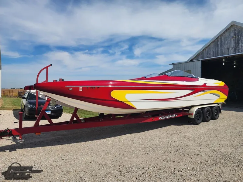 Slide: The Image of Red and yellow 2005 Eliminator Daytona 30 speedboat on trailer, parked near a barn. - 3