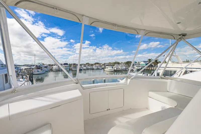 Slide: The Image of 1999 Viking 55 Convertible yacht interior with marina view, featuring white seating and clear skies. - 16