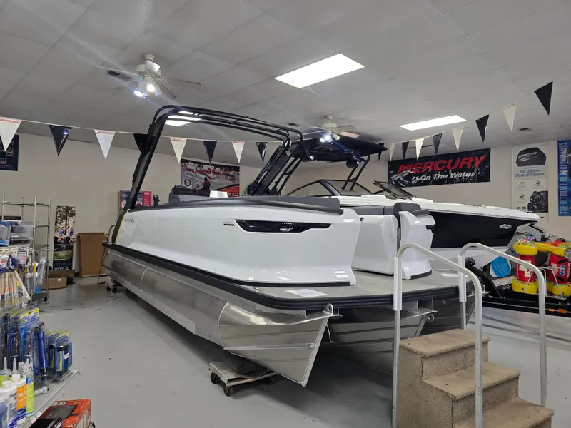 Slide: The Image of 2025 Manitou Explore Navigator pontoon boat displayed in a showroom with accessories. - 0