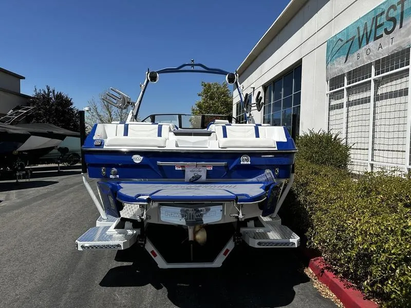 Slide: The Image of 2025 Malibu Wakesetter 23LSV boat, blue and white, parked outside West Boat dealership. - 2