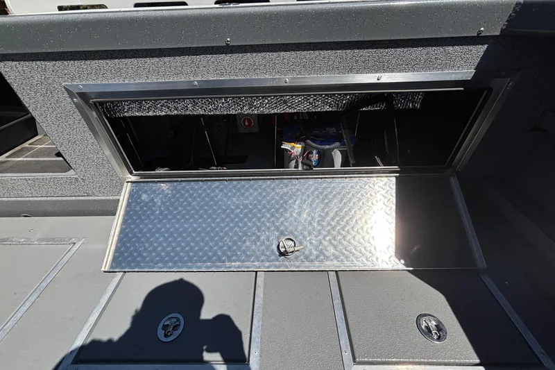 Slide: The Image of Open storage compartment on 2025 Spartan 2600 Olympia boat, featuring diamond plate cover. - 18