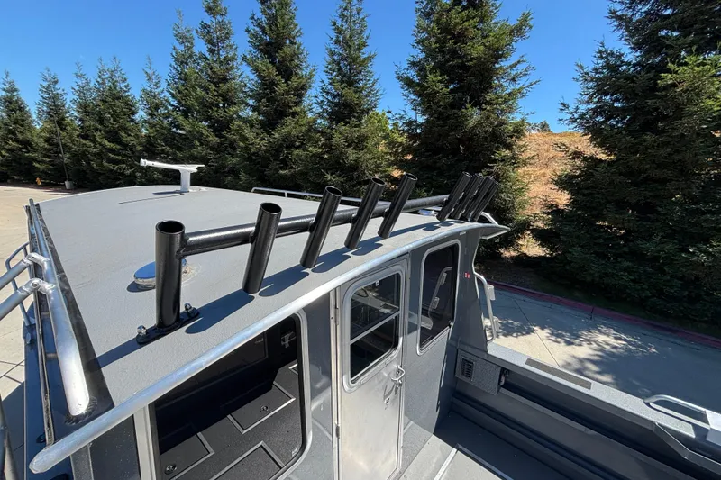 Slide: The Image of Rooftop view of 2025 Spartan 2600 Olympia boat with rod holders, surrounded by trees. - 10