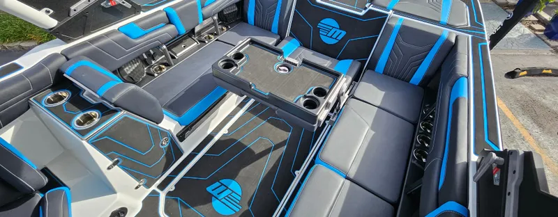 Slide: The Image of 2025 Malibu 25LSV boat interior with blue and black seating, cup holders, and sleek design. - 10