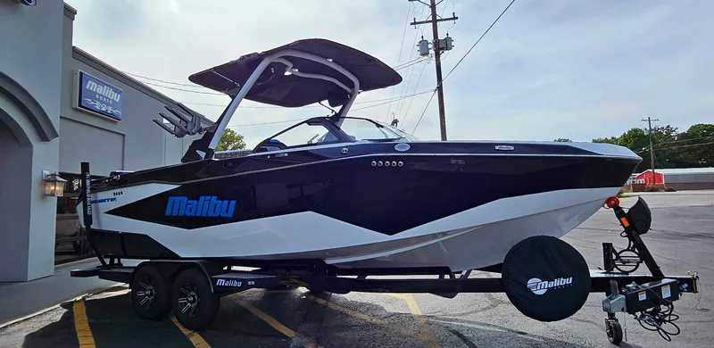 Slide: The Image of 2025 Malibu 25LSV boat on trailer, sleek black and white design, parked outside dealership. - 4