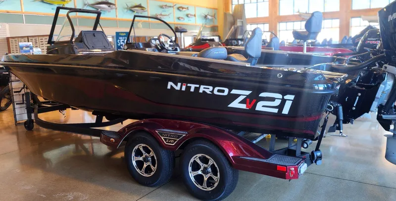 The Image of 2024 Nitro ZV21 boat on display in showroom, featuring sleek design and dual-axle trailer. - 0