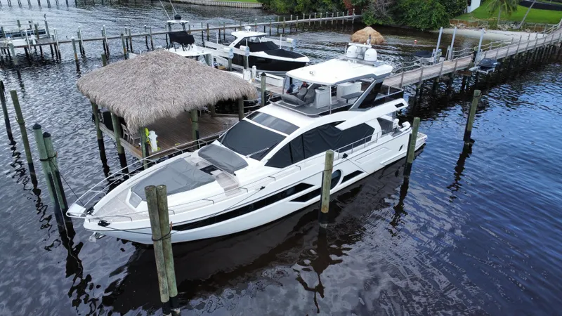 Slide: The Image of 2024 Aicon 66 Vivere yacht docked at a marina with thatched roof hut. - 6