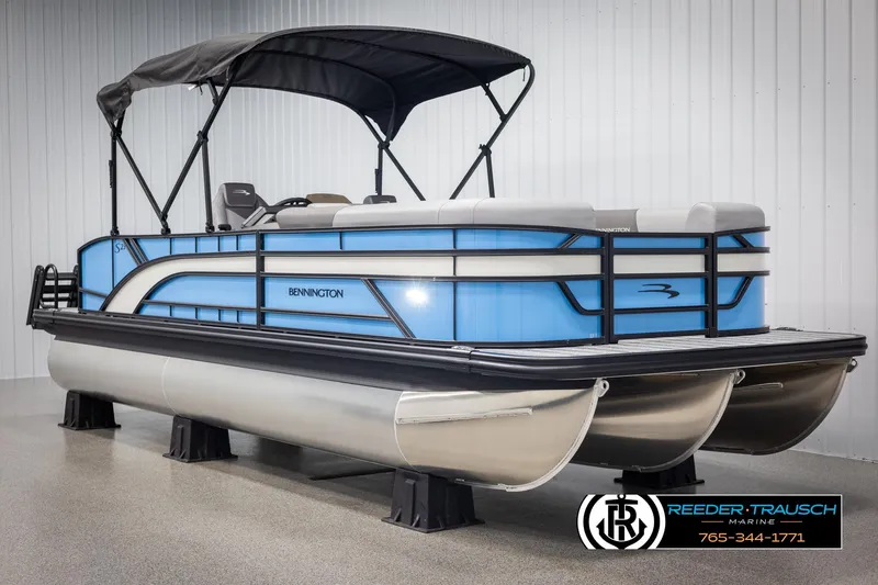 Slide: The Image of 2025 Bennington 23 SSBSE pontoon boat with blue accents and canopy in showroom. - 3