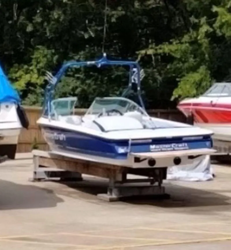 Slide: The Image of 2003 MasterCraft ProStar 197 boat on a trailer, surrounded by trees and other boats. - 6