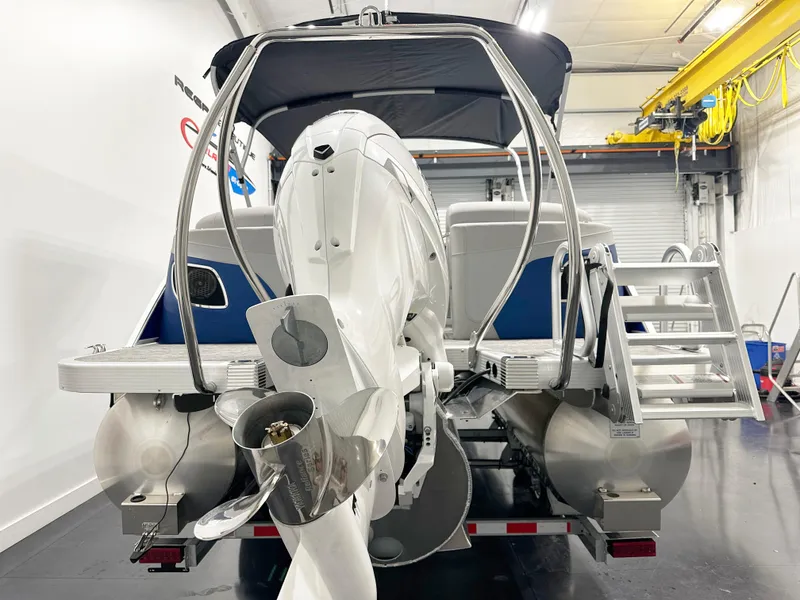 Slide: The Image of 2025 Bennington 23LFBCSR pontoon boat in a garage, rear view with motor and ladder. - 5