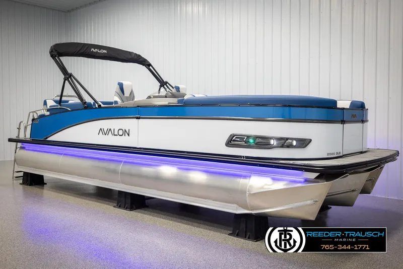 Slide: The Image of 2025 Avalon Catalina QLS pontoon boat with blue accents and LED lighting in showroom. - 2