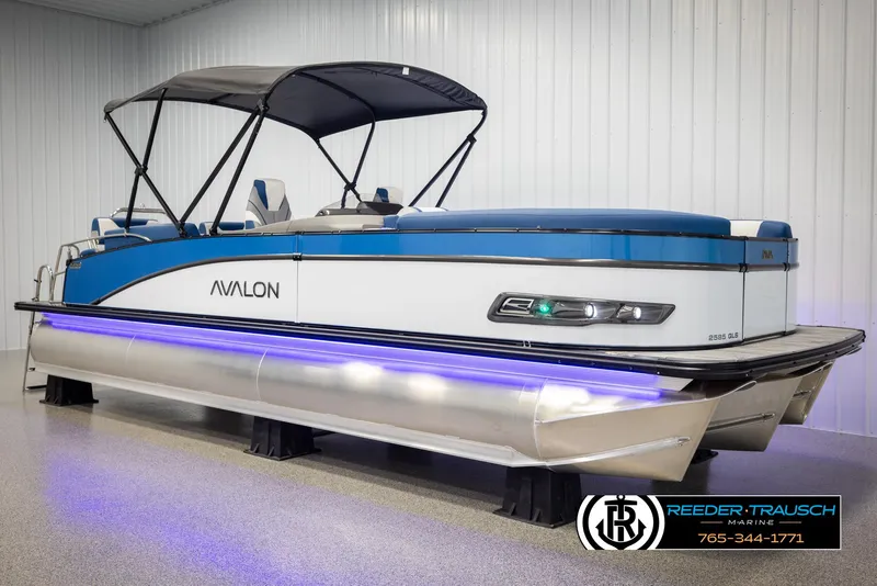Slide: The Image of 2025 Avalon Catalina QLS pontoon boat with blue accents and canopy in showroom. - 3