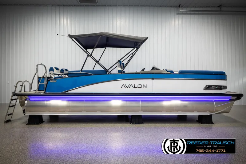 Slide: The Image of 2025 Avalon Catalina QLS pontoon boat with blue accents and canopy in showroom. - 5