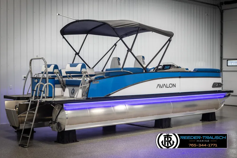 Slide: The Image of 2025 Avalon Catalina QLS pontoon boat with blue accents and canopy in showroom. - 6