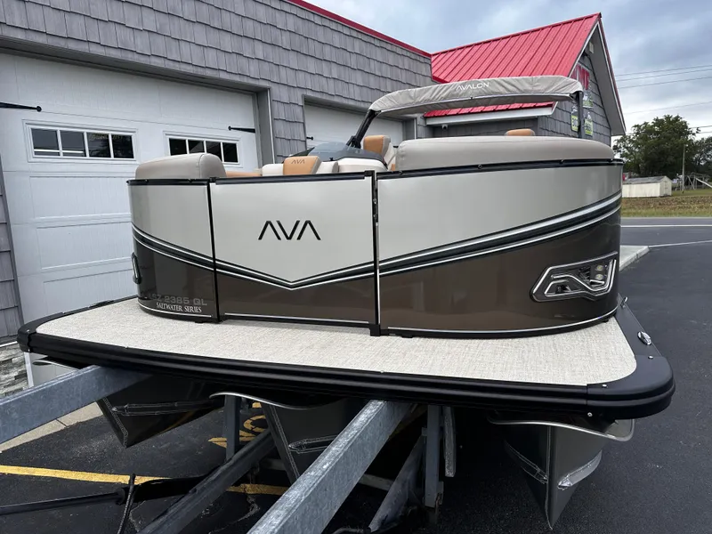 Slide: The Image of 2025 Avalon 2385 LSZ Quad Lounger Tri Toon boat on trailer, parked near garage. - 2
