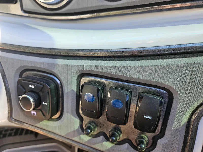 Slide: The Image of Dashboard controls of 2023 Sanger V215 LTZ boat, featuring switches and knobs. - 19