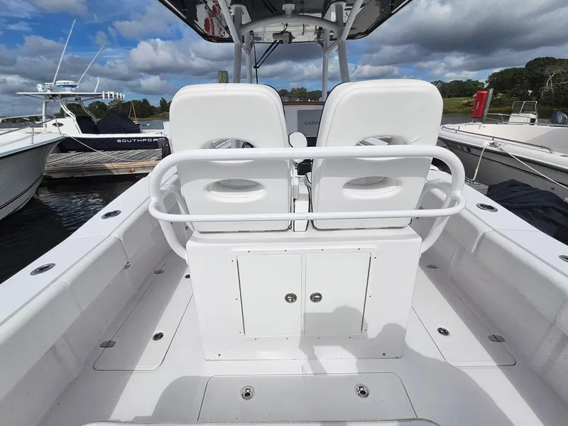 Slide: The Image of 2022 Southport 27 FE boat interior with white seating and storage, docked under a cloudy sky. - 12