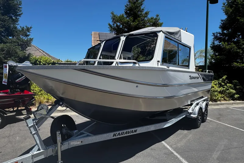 Slide: The Image of 2024 Spartan 215 Athens boat on trailer, parked outdoors under clear blue sky. - 2