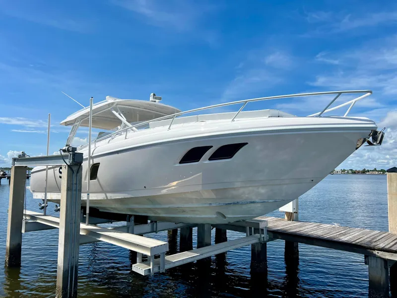 Slide: The Image of 2018 Intrepid 407 Cuddy boat on lift, docked by the water under a clear blue sky. - 6