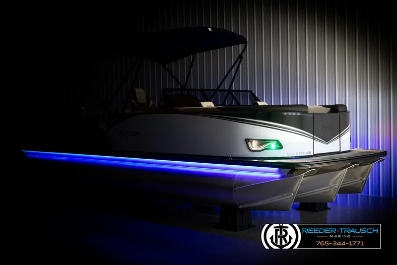 Slide: The Image of 2025 Avalon LSZ VRB pontoon boat with blue LED lights in a dimly lit showroom. - 4