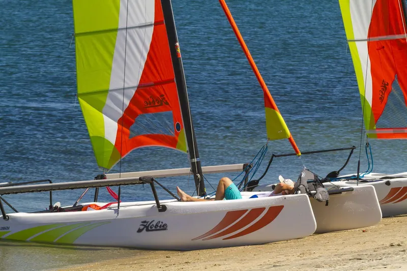 Slide: The Image of 2024 Hobie Cat Getaway sailboats on sandy beach with colorful sails. - 8