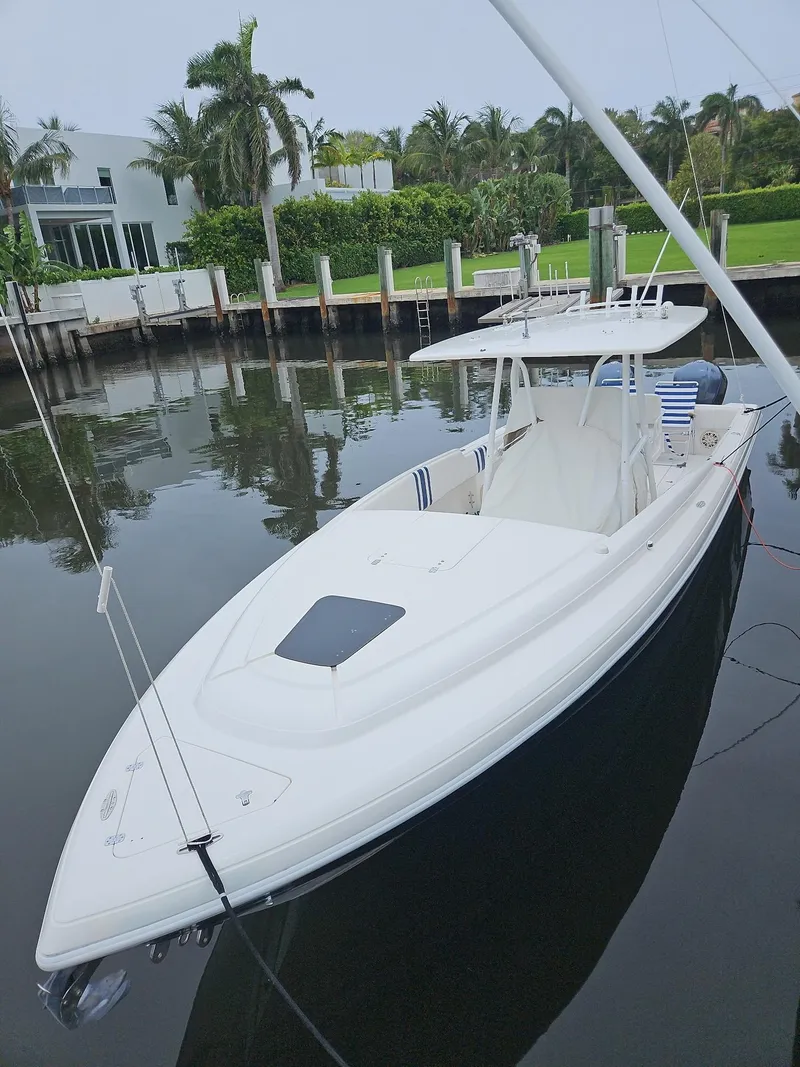 Slide: The Image of 2005 Intrepid 323 Cuddy boat docked by waterfront with lush greenery and modern architecture. - 17