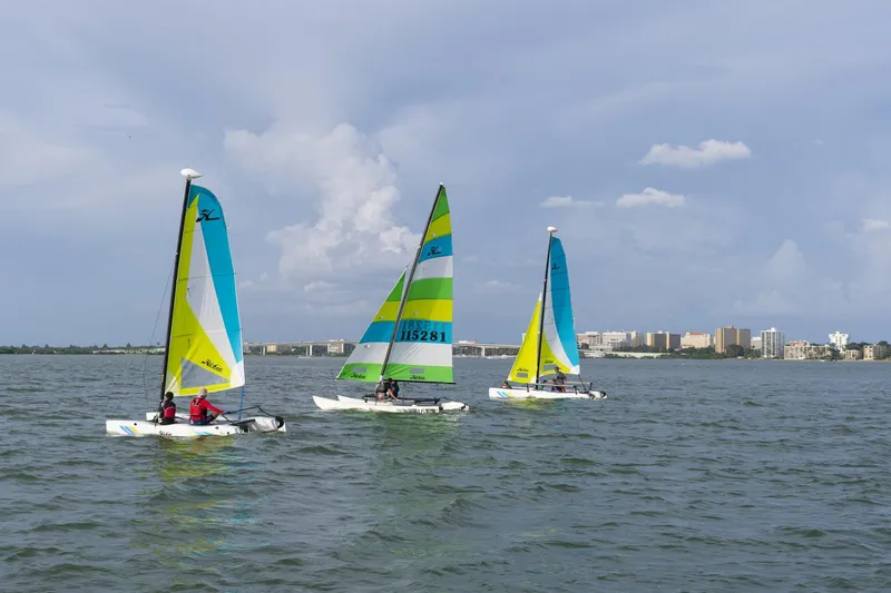 Slide: The Image of Three 2025 Hobie Cat 16 catamarans sailing on a calm sea under a partly cloudy sky. - 5