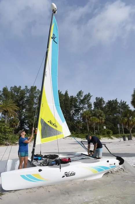 Slide: The Image of 2024 Hobie Cat Club WAVE sailboat on sandy beach with two people setting up. - 2