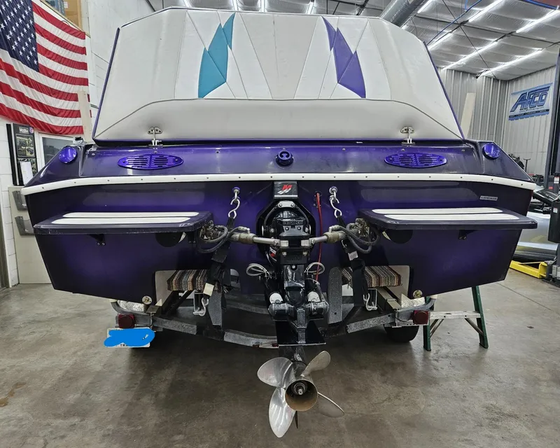 Slide: The Image of 2000 Eliminator 25 Daytona boat, rear view in a garage, featuring a purple hull and American flag. - 13